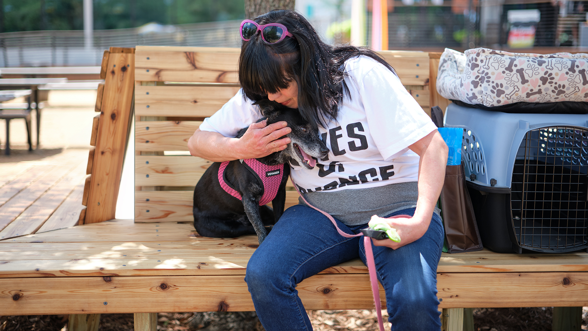 A woman hugs small black dog on wooden bench next to a small dog crate.
